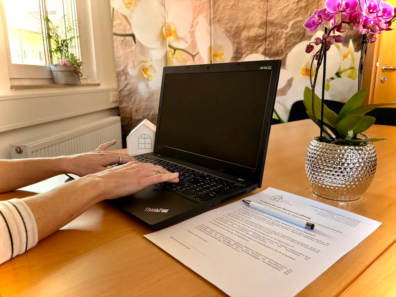 Patzina Immobilienverwaltung GmbH- Frau tippt auf ihrem Laptop, neben ihr liegt ein Vertragsdokument auf dem Tisch